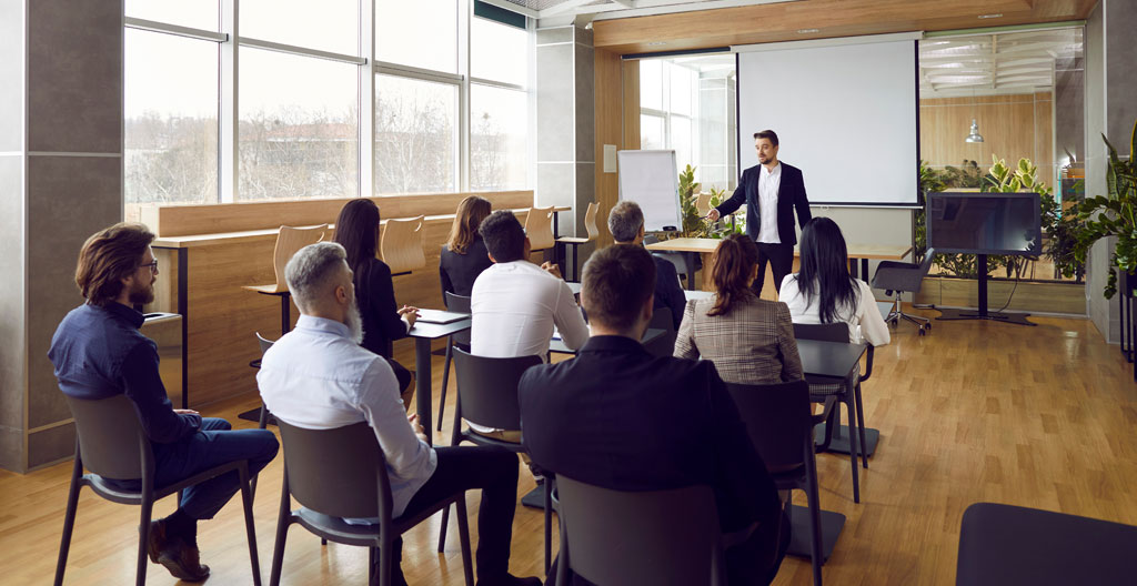 Session de formation en petit groupe vue de dos, formateur debout face aux participants dans une salle lumineuse et moderne