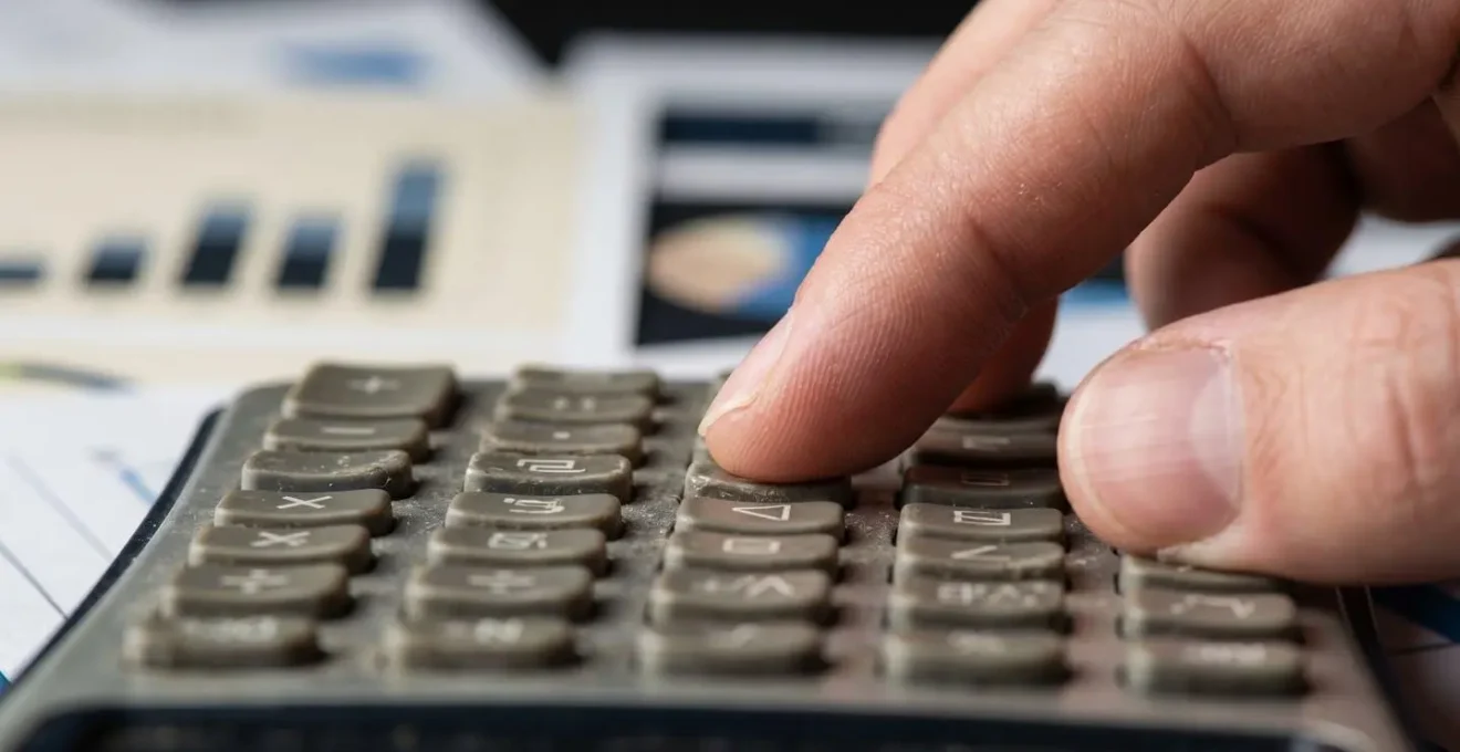 Gros plan sur des mains manipulant une calculatrice professionnelle avec des documents financiers flous en arrière-plan