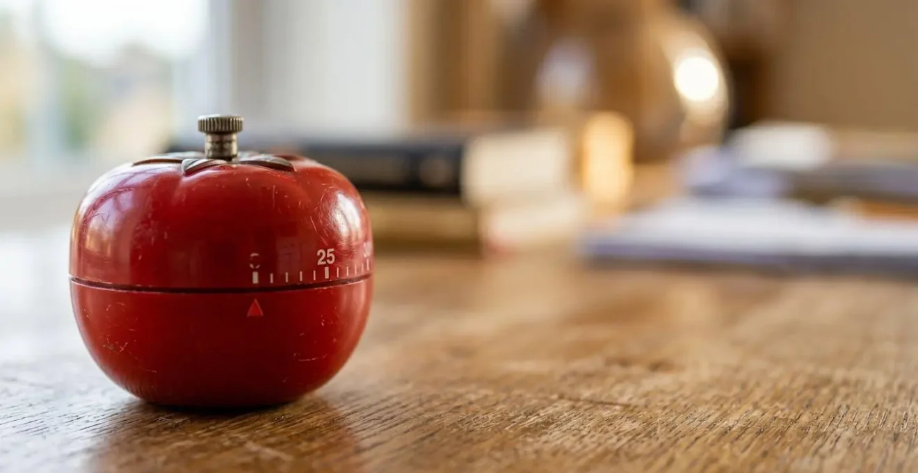 Gros plan sur un minuteur de cuisine rouge en forme de tomate posé sur un bureau d'étudiant avec des livres flous en arrière-plan